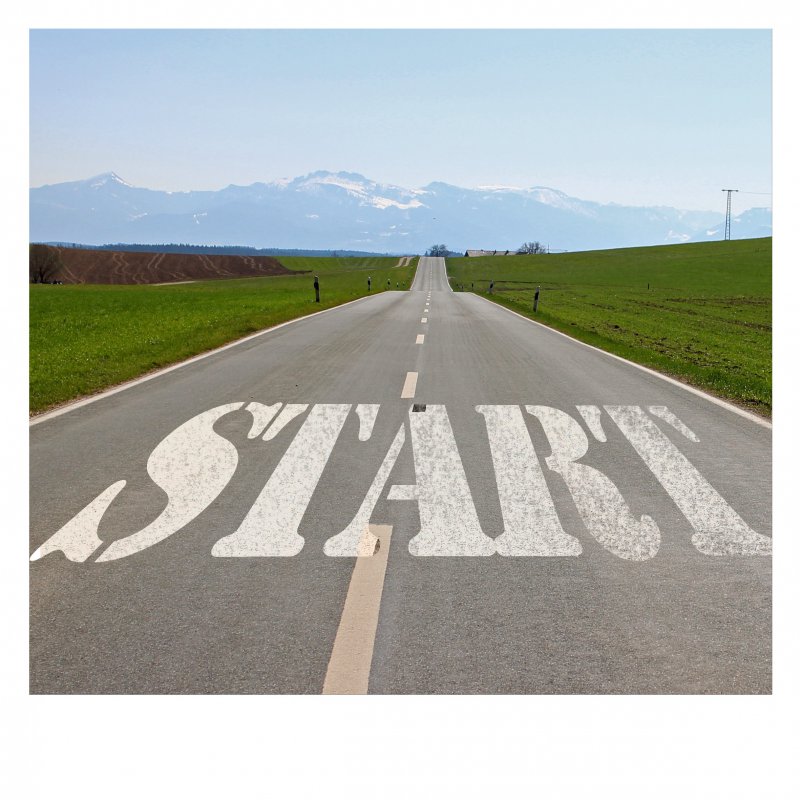 Das Wort &quot;Start&quot; steht auf einer Straße, die geradeaus führt. Die Landschaft ich hügelig, im Hintergrund sind Berge zu sehen.